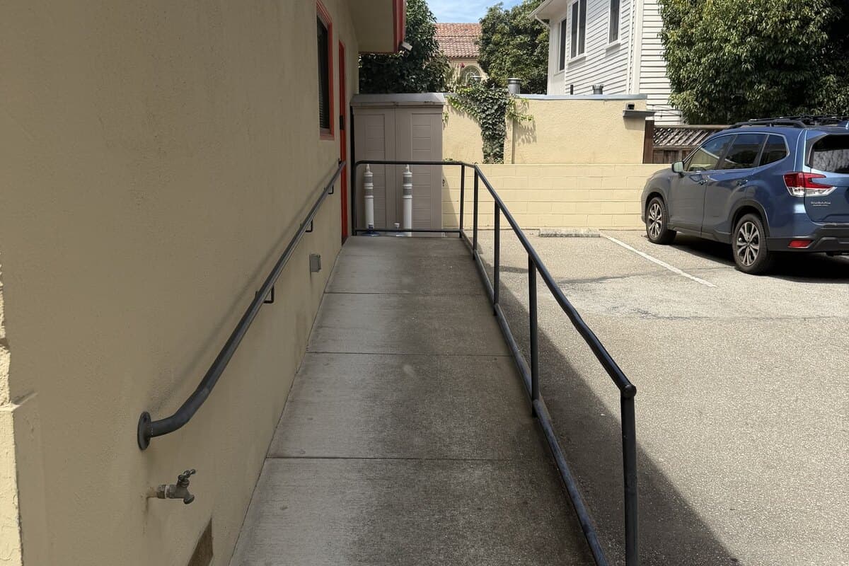 A concrete ramp with a metal handrail running from the parking lot along the side of the office building.