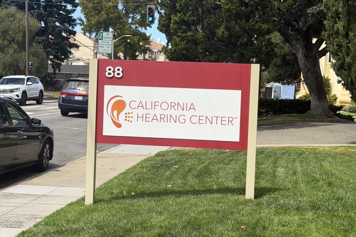A red-and-white California Hearing Center sign reading 88, standing on a lawn beside the sidewalk on N. San Mateo Drive.
