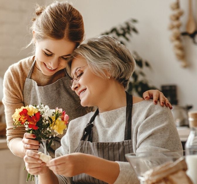 An adult daughter hugs her mother in a kitchen